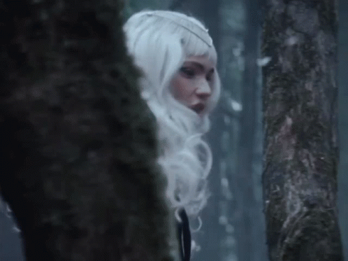A Woman In A White Wig Is Standing In A Dark Forest GIF