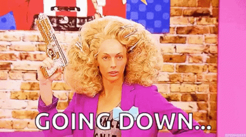 A Woman In A Wig Is Holding A Gun In Front Of A Brick Wall And Says `` Going Down '' . GIF