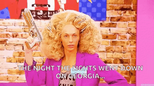 A Woman In A Wig Is Holding A Gun In Her Hand . GIF