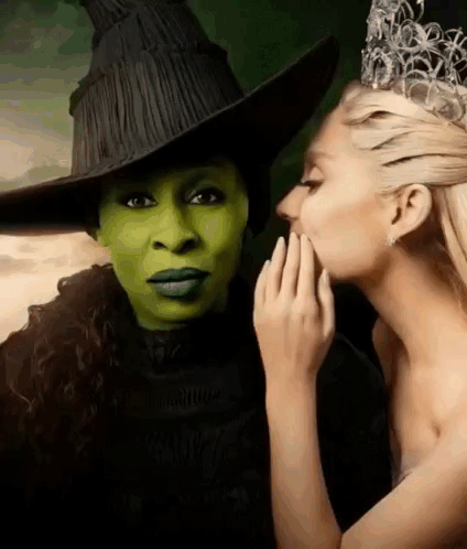 A Woman In A Witch Costume Is Whispering Into The Ear Of Another Woman In A Crown . GIF
