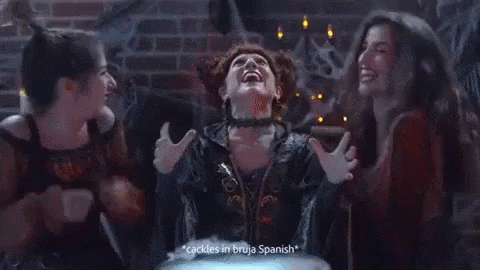 A Woman In A Witch Costume Says " Cackles In Bruja Spanish " While Two Other Women Look On GIF