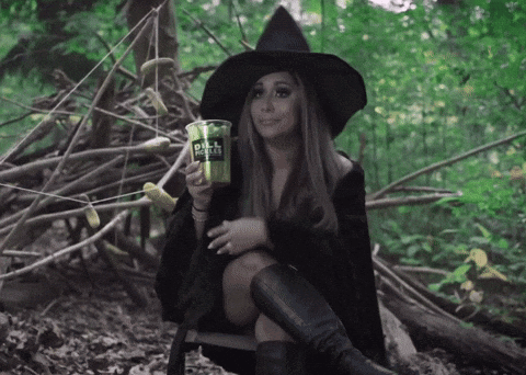 A Woman In A Witch Costume Sits In The Woods Holding A Cup That Says Dill Coffee GIF