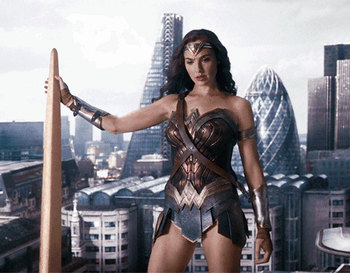 A Woman In A Wonder Woman Costume Holds A Sword In Front Of A City Skyline GIF