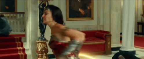 A Woman In A Wonder Woman Costume Is Holding A Lightning Bolt GIF