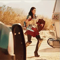 A Woman In A Wonder Woman Costume Is Holding A Shield And Sword While Walking Towards A Van . GIF