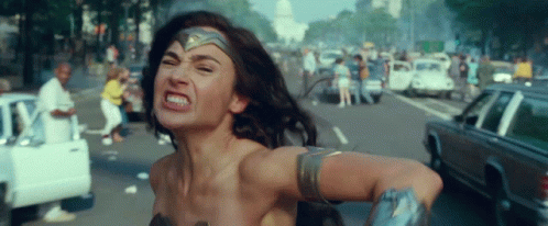 A Woman In A Wonder Woman Costume Is Running Down A Street With Cars . GIF
