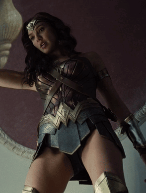 A Woman In A Wonder Woman Costume Is Standing In Front Of A Purple Wall GIF