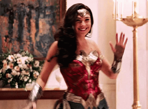 A Woman In A Wonder Woman Costume Is Waving Her Hand And Smiling . GIF