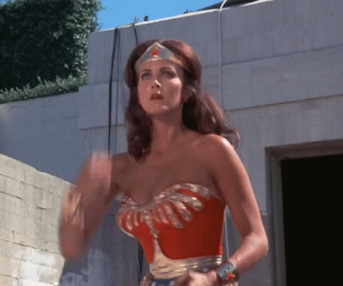A Woman In A Wonder Woman Costume Is Waving GIF