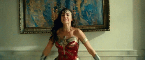 A Woman In A Wonder Woman Costume Stands In Front Of A Framed Picture GIF