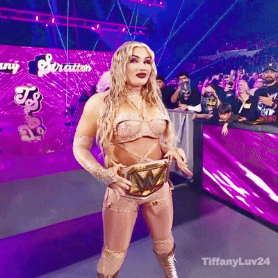 A Woman In A Wrestling Outfit Is Standing In Front Of A Purple Wall That Says Tiffanyluv24 GIF