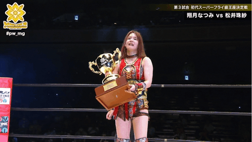 A Woman In A Wrestling Ring Holds A Trophy In Front Of A Referee With #Pw_mg Written On The Bottom GIF
