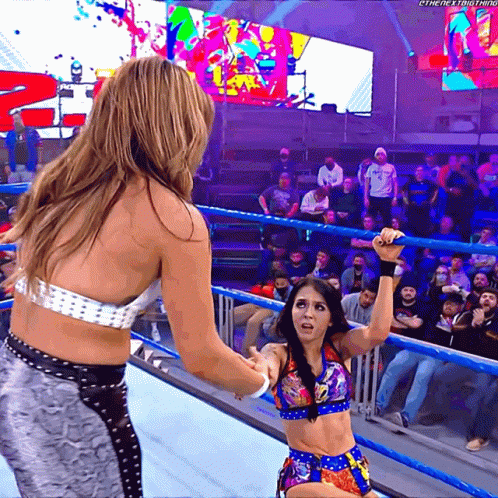 A Woman In A Wrestling Ring Holds Another Woman 'S Hand In Front Of A Crowd That Is Watching GIF