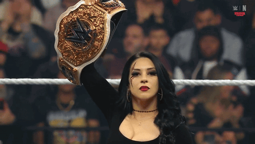 A Woman In A Wrestling Ring Holds Up A Gold Wrestling Championship Belt GIF