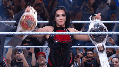 A Woman In A Wrestling Ring Holds Up Two Belts In Front Of A Crowd GIF