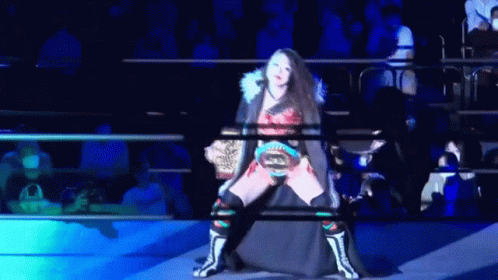 a woman in a wrestling ring is holding a belt that says champion