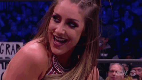 A Woman In A Wrestling Ring Is Smiling In Front Of A Crowd Of People . GIF