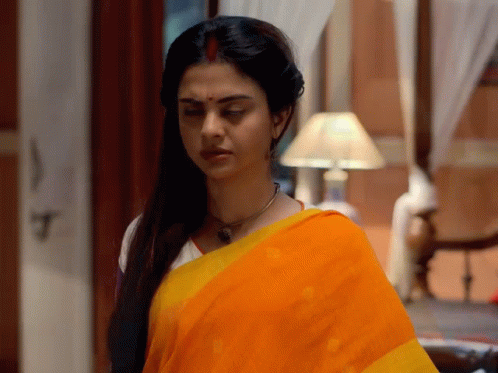 A Woman In A Yellow And Orange Saree Is Standing In A Room GIF