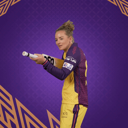 A Woman In A Yellow And Purple Jersey Holding A Dsc Bat GIF