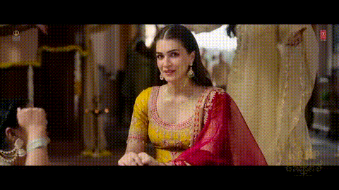 A Woman In A Yellow And Red Dress Is Standing In Front Of A Man . GIF