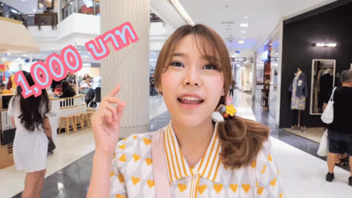 A Woman In A Yellow And White Shirt Points To A Sign That Says 1,000 บาท GIF