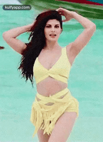 A Woman In A Yellow Bikini Is Standing In A Pool Of Water . GIF