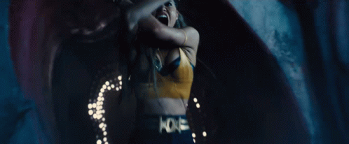 A Woman In A Yellow Bra Is Dancing In A Dark Room With A Blue Background . GIF