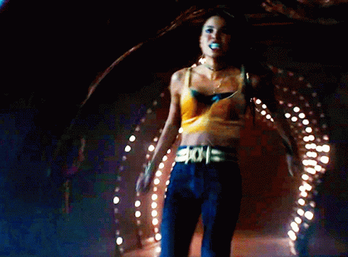 A Woman In A Yellow Crop Top Is Holding Another Woman In A Dark Room GIF