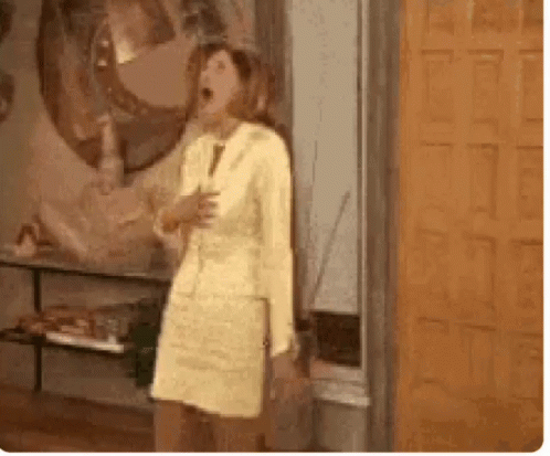 A Woman In A Yellow Dress And Suit Is Standing In Front Of A Door . GIF