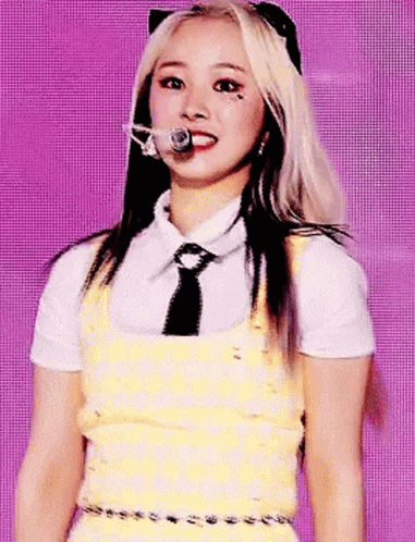 A Woman In A Yellow Dress And Tie Is Standing In Front Of A Microphone . GIF