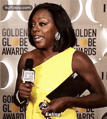A Woman In A Yellow Dress Is Holding A Microphone And Talking Into It At The Golden Globe Awards . GIF