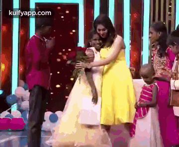 A Woman In A Yellow Dress Is Hugging A Little Girl In A White Dress On A Stage . GIF