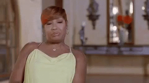 A Woman In A Yellow Dress Is Making A Funny Face In A Room . GIF