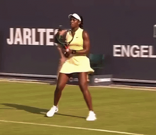 A Woman In A Yellow Dress Is Playing Tennis On A Court GIF