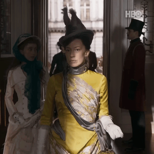 A Woman In A Yellow Dress Is Standing In A Doorway With A Hbo Logo In The Background GIF