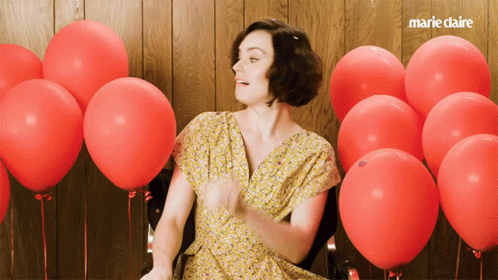 A Woman In A Yellow Dress Is Surrounded By Red Balloons And The Words Marie Claire Are On The Bottom GIF