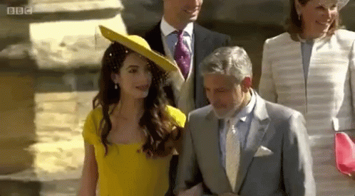 A Woman In A Yellow Dress Is Walking With A Man In A Suit And Tie . GIF