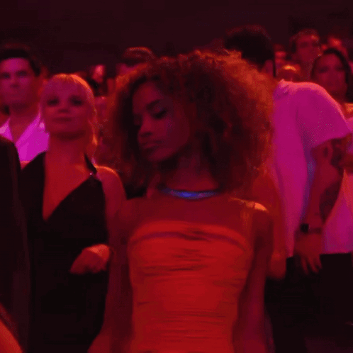 A Woman In A Yellow Dress Stands In A Crowd Of People GIF