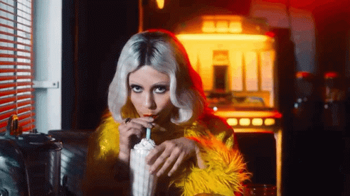 A Woman In A Yellow Fur Coat Drinking A Milkshake Through A Straw . GIF
