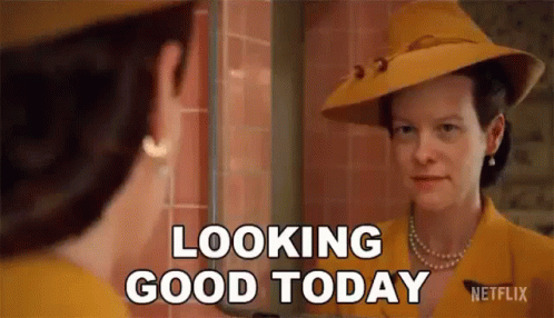 A Woman In A Yellow Hat Is Looking At Her Reflection In A Mirror And Saying `` Looking Good Today '' . GIF