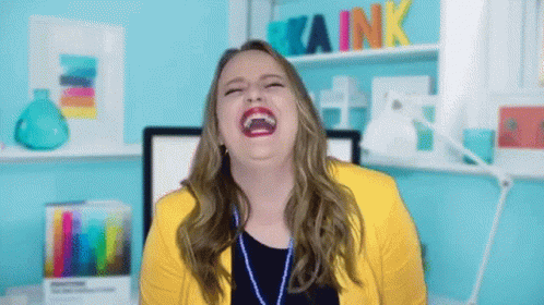 A Woman In A Yellow Jacket Is Laughing In Front Of A Kaink Sign GIF