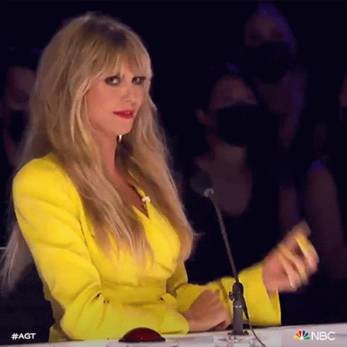 A Woman In A Yellow Jacket Is Sitting At A Table With A Microphone In Front Of Her . GIF