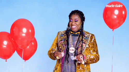 A Woman In A Yellow Jacket Is Surrounded By Red Balloons And Has A Cinc Necklace Around Her Neck GIF