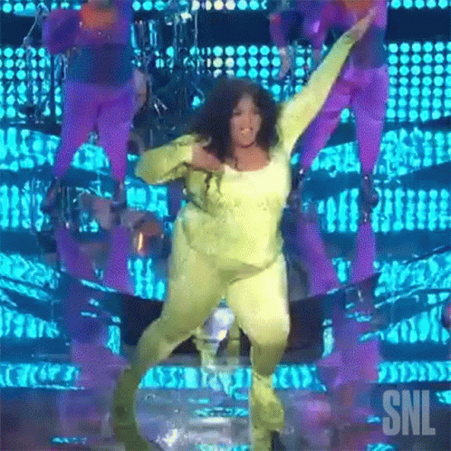 A Woman In A Yellow Jumpsuit Is Dancing On A Stage With Snl Written On The Bottom GIF