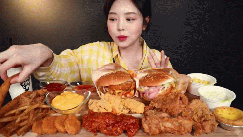 A Woman In A Yellow Plaid Shirt Is Eating A Lot Of Fried Food GIF