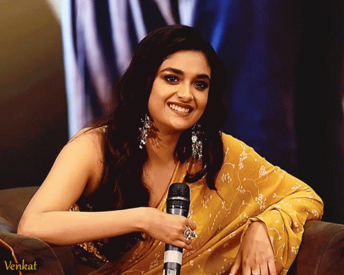 a woman in a yellow saree is smiling while holding a microphone and the word venkat is on the bottom right