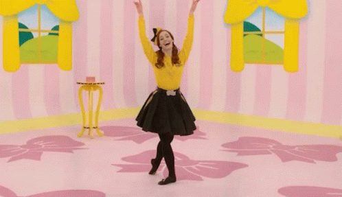 A Woman In A Yellow Shirt And Black Skirt Is Dancing In A Pink Room GIF