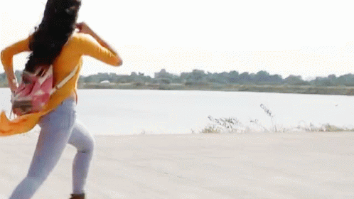 A Woman In A Yellow Shirt And Blue Jeans Is Running With A Pink Backpack GIF