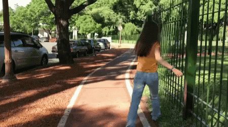 A Woman In A Yellow Shirt And Blue Jeans Is Walking Down A Bike Path GIF