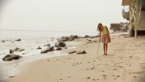 A Woman In A Yellow Shirt And Pink Skirt Is Walking Along The Beach GIF